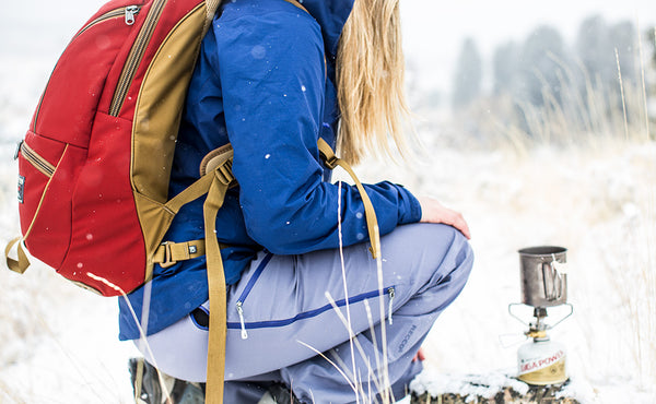 A person using a camp stove in the snow while wearing a Guide's Edition Synapse 25.